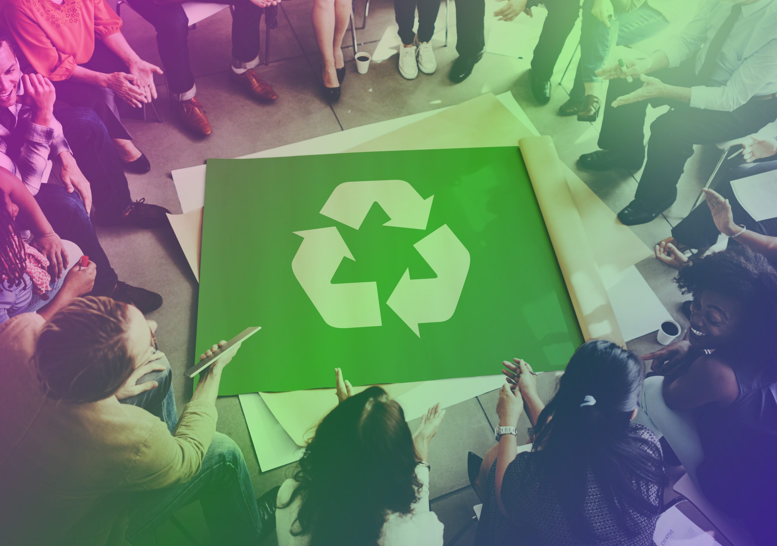 A group of business people in an organisation sat around a recycle sign on the issue of disposal of devices in an environmentally-friendly way.